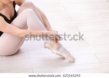 Ballet art concept. Young beautiful ballerina tying point shoes on floor