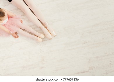 Ballet background. Little girl and young ballerina legs in pointe shoes on white wooden floor, top view from above with copy space. Classical dance school background, practicing for children