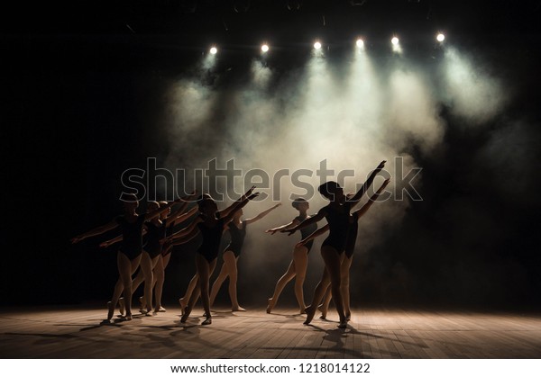 Ballet class\
on the stage of the theater with light and smoke. Children are\
engaged in classical exercise on\
stage.
