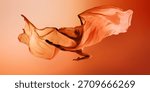 Ballet dancer floating under large orange fabric wave on warm background. Concept of campaign visuals, airy dance moments, editorial movement photography.