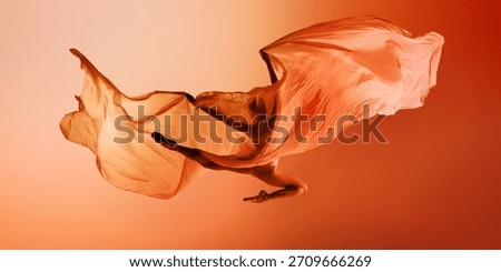 Ballet dancer floating under large orange fabric wave on warm background. Concept of campaign visuals, airy dance moments, editorial movement photography.