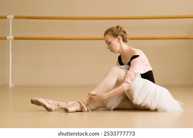 A ballet dancer sitting on the studio floor adjusting her pointe shoes, in a calm, focused moment after practice. - Powered by Shutterstock