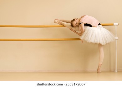 A ballet dancer stretches by placing her leg on the barre while resting her body, wearing a pink cardigan over her tutu. - Powered by Shutterstock