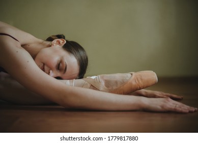 Ballet Dancer Warming Up In Studio. Graceful Ballerina In Pointe Shoes On The Brown Wooden Floor. Ballet Practice And Stretching. Female Stretching Indoors Toes Professional Arts. Copy Space