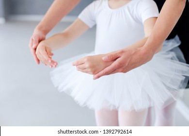 Ballet Teacher Helps Little Ballerina In Classical Dance School. Female Dance Trainer Is Teaching Kid Girl To Do Choreographic Position With Hands. Practicing For Children. Close Up.