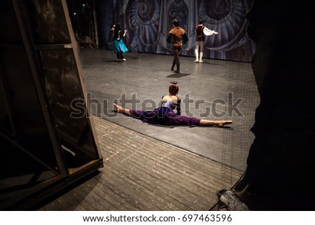 ballet, theater, background. on backstage of theater dancers are rehearsing, ballerina dressed in gorgeous costume in purple shades and with red hair doing the splits nearby decoration