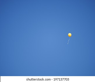 A balloon on a string floating in a cloudless sky.