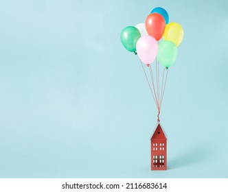 Balloons of different colors attached to a house ona a blue background. Minimal concept.