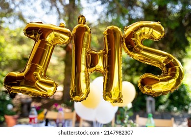 Balloons In The Shape Of The Letters IHS, Referring To The Sacrament Of First Holy Communion. In The Background, An Outdoor Party For Children. IHS 