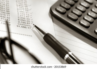 Ballpoint Pen With Calculator And Glasses On Financial Spreadsheet With Columns And Rows Of Numbers Checked With Check Marks After Account Reconciliation