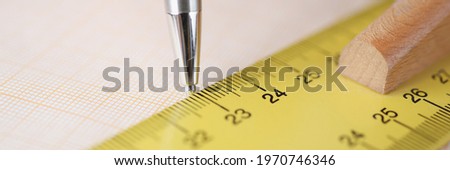 Ballpoint pen drawing line under ruler on graph paper closeup