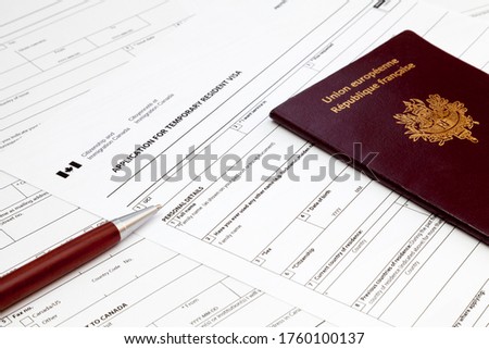 A ballpoint pen and a French passport on the top of an Canadian temporary resident visa application form.