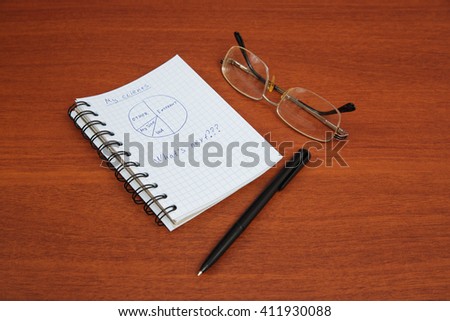 ballpoint pen, glasses and an open notebook lying on the table