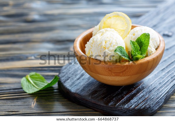 Balls of lemon ice cream, mint and slice\
of lemon in a wooden bowl, selective\
focus.