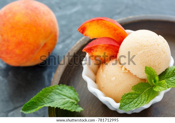 Balls peach ice cream and mint leaves in bowl on\
wooden plate, selective\
focus.