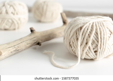 Balls of white yarn and rustic sticks on white table. Threads of wool boho image.Good for macrame and handicrafts banners and advertisement
