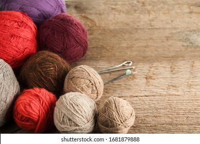 Balls of yarn in different colors with knitting needles on a background of rough wood texture. Selective focus.