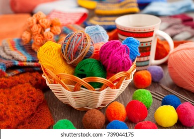 Balls of yarn for knitting. Balls of yarn for knitting in a wicker basket. A cup of tea, a knitting yarn, knitted clothes create coziness. Colorful multi-colored yarn for knitting.