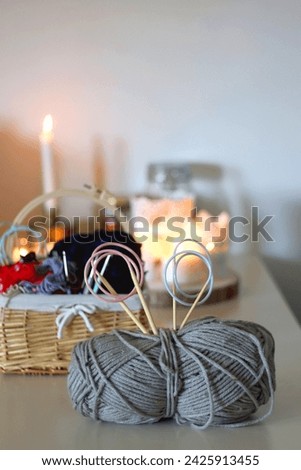 Balls of yarn, threads, various needlecraft needles and lit candles on the table. Hygge at home. Selective focus.
