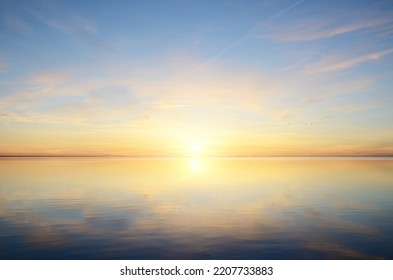 Baltic sea after the rain. Dramatic sunset sky, glowing pink and golden clouds, symmetry reflections in the water. Abstract natural pattern, texture, background. Picturesque panoramic scenery