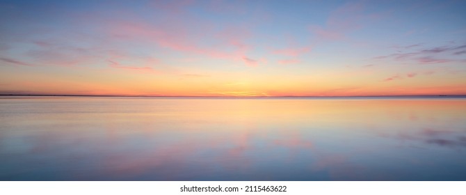 Baltic sea. Dramatic sunset sky, glowing pink and golden clouds, symmetry reflections in the water. Abstract natural pattern, texture, background. Picturesque panoramic scenery