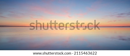 Baltic sea. Dramatic sunset sky, glowing pink and golden clouds, symmetry reflections in the water. Abstract natural pattern, texture, background. Picturesque panoramic scenery