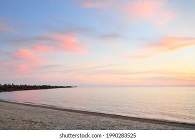 Baltic sea shore under a blue sky with glowing pink and golden sunset clouds. Rocky shore, breakwaters. Idyllic seascape. Latvia. Nature, environmental conservation, ecotourism. Picturesque scenery