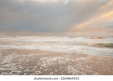 Baltic sea at sunset. Dramatic sky, blue and pink glowing clouds, golden sunlight. Waves, splashing water. Picturesque scenery, seascape, nature. Panoramic view, long exposure