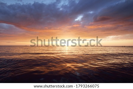 Baltic sea at sunset. Dramatic sky with glowing clouds reflecting in the water. Lighthouse in the background. Setting sun. Epic seascape. Abstract natural pattern, texture, background, concept image