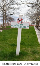 Baltimore, Maryland US - April 9, 2022: Grass park along Fells Point waterfront with green grass and a white cross shaped sign that reads "Please No dogs on grass, pet waste" 