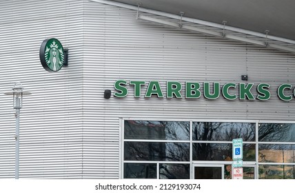 Baltimore, Maryland US - February 24, 2022: Starbucks Seattle Based Coffee Shop Chain Logo And Light Up Text Sign Above Corrugated Metal Building Exterior At Busy Downtown Location