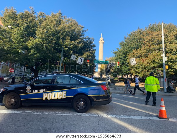 Baltimore, MD / US - Oct 19, 2019: Baltimore\
Maryland Running festival Marathon 5k downtown. City police squad\
car and officer block St Paul st as runner pass cop and the\
Washington monument