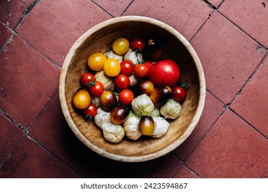 Bamboo bowl full of fresh red and yellow cherry tomatoes and tomatillos, on the red and brown tiled floor - Powered by Shutterstock