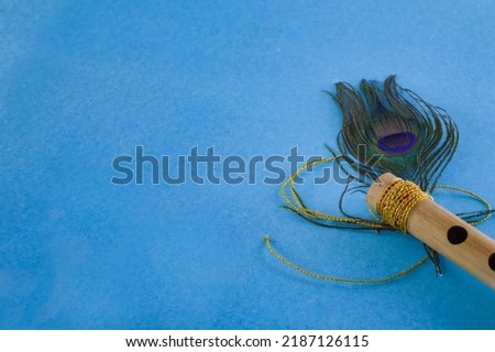 Bamboo flute decorated with peacock feather symbolic to hindu god lord krishna during celebration of janmashtami festival. photo taken in blue background with copy space.
