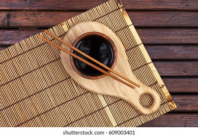 Bamboo Mat, Soy Sauce, Chopsticks On Dark Wooden Table. Top View With Copy Space