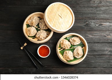 Bamboo steamers with tasty baozi dumplings, chopsticks and bowl of sauce on wooden background, top view