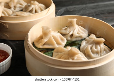 Bamboo steamers with tasty baozi dumplings and bowl of sauce on table