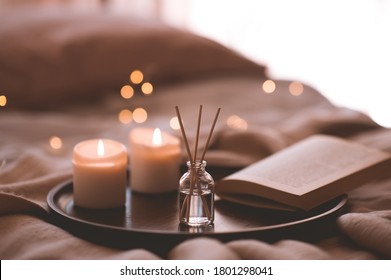 Bamboo sticks in bottle with scented candles and open book on wooden tray in bed closeup. Home aroma. 