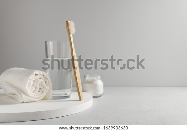 Bamboo toothbrush, glass of water, white a\
cotton towel and powder for brushing your teeth in jar. light gray\
concrete surface, gray backdrop. Biodegradable personal care\
products. No plastic\
concept.