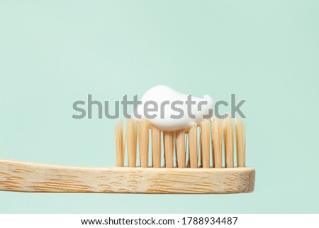 Bamboo toothbrush with toothpaste on mint background with copy space. Close up view in sunlight.