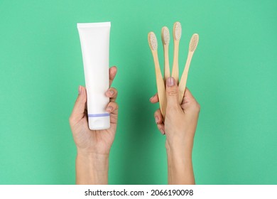 Bamboo Toothbrushes And A Tube Of Toothpaste In Female Hands On A Mint Background. Current Trends In Conscious Consumption.