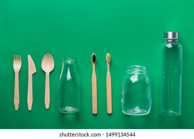 Bamboo toothbrushes wooden cutlery glass bottle jar on green background. Zero waste plastic free eco friendly reusable materials. Poster banner knolling flat lay