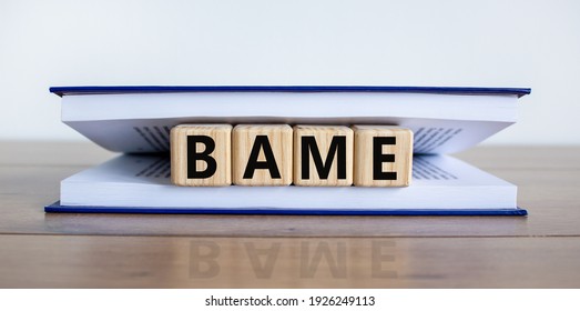 BAME Symbol. Abbreviation BAME, Black, Asian And Minority Ethnic On Wooden Cubes In Book. Beautiful White Background. Copy Space. Business And BAME, Black, Asian And Minority Ethnic Concept.