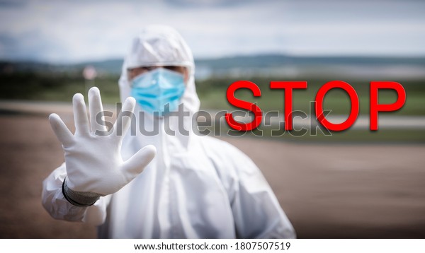 Ban on movement of cars on border of cities\
due to pandemic coronavirus COVID 19 or Bubonic Plague, man in\
biological protective suit shows stop\
gesture.