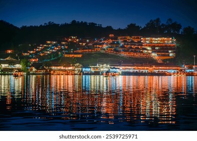 Ban Rak Thai village glows in the night with vibrant lights reflecting on the lake, creating a scenic and tranquil view of traditional architecture and hills. - Powered by Shutterstock