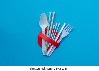 Ban single use plastic. A creative artwork of stop/prohibition sign over colorful plastic cotton bud, straw, stirrer, fork, spoon on blue background. Environmental concept.