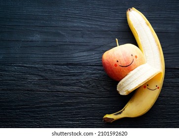 Banana and apple, smilies, lie on a black background