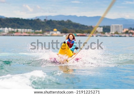 Banana boat ride. Summer vacation fun. Kids play on the beach. Island resort activity. Tropical holiday. Children enjoy water raft.