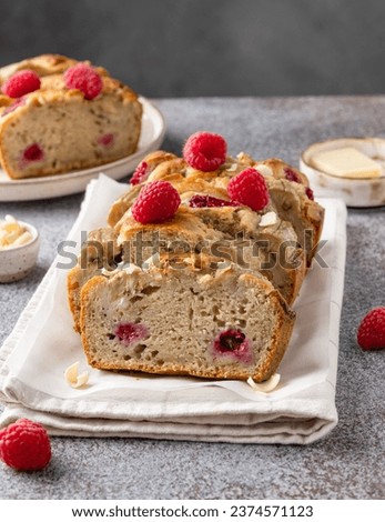 Banana bread with fresh raspberry and white chocolate. Fruit loaf cake sliced in pieces and served on kitchen napkin. Vegan breakfast, dessert or lunch. Grey concrete table. Close up view.