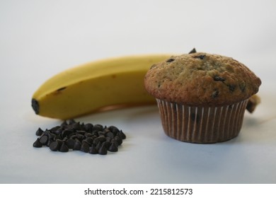 Banana Chocolate Chip Muffin With Banana And Small Pile Of Chocolate Chips.